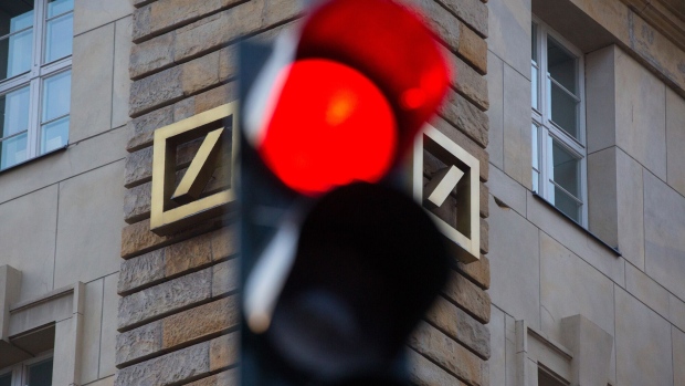 A red road traffic light stands illuminated as the logo of Deutsche Bank AG sits on the exterior of the bank's offices in Berlin, Germany, on Wednesday, Sept. 28, 2016. Deutsche Bank AG rose in Frankfurt trading after the German lender agreed to sell its U.K. insurance business for 935 million euros ($1.2 billion) and Chief Executive Officer John Cryan ruled out a capital increase. Photographer: Krisztian Bocsi/Bloomberg