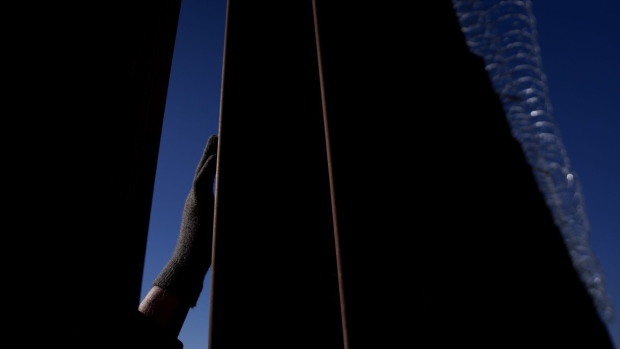 A migrant touches the border wall while waiting at the US and Mexico border in El Paso, Texas, US, on Thursday, Dec. 22, 2022. Chief Justice John Roberts temporarily blocked the scheduled ending of pandemic-era border restrictions while the US Supreme Court considers a bid by Republican state officials to keep the rules in place during a legal fight. Photographer: Eric Thayer/Bloomberg