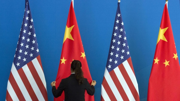 A Chinese woman adjusts a Chinese flag near US flags before the start of a Strategic Dialogue expanded meeting between China and the US during the US-China Strategic and Economic Dialogue held at the Diaoyutai State Guesthouse in Beijing on July 10, 2014. Photographer: NG HAN GUAN/AFP
