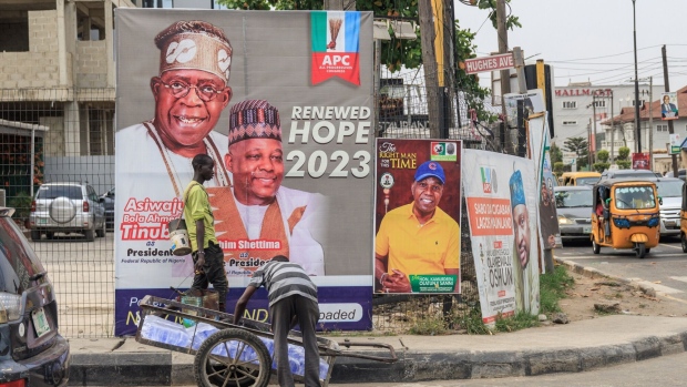 A worker arranges bags of water onto a cart in front of election posters for the All Progressive Congress (APC) presidential candidate Bola Tinubu and his running mate Kashim Shettima in the Yaba district of Lagos, Nigeria, on Monday, Feb. 6, 2023. Nigerians are gearing up to choose a successor to President Muhammadu Buhari, whose eight years in power have been blighted by economic decay, soaring unemployment, heightened insecurity and an exodus of the educated elite. Photographer: Benson Ibeabuchi/Bloomberg