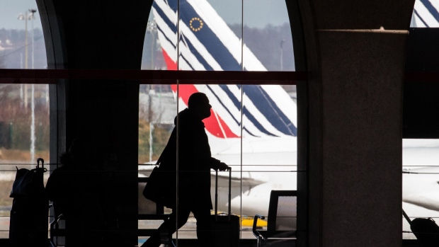 A passenger walks through the terminal as Tricolour livery sits on the tail fin of an Air France passenger aircraft beyond, operated by Air France-KLM Group, as it stands on the tarmac at Charles de Gaulle airport, operated by Aeroports de Paris, in Paris, France, on Monday, Feb. 12, 2018. Air France will report its full year earnings on Feb 16.