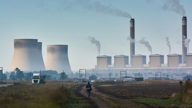 A pedestrian walks through a field, backdropped by the Eskom Holdings SOC Ltd. Kendal coal-fired power station in Mpumalanga, South Africa, on Friday, May 5, 2023. Debt-strapped Eskom is currently implementing daily blackouts because its dilapidated power plants are unable to supply enough electricity to meet demand and it doesn’t have the money to invest in capital equipment.