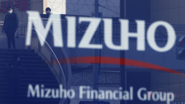 Pedestrians are reflected in signage for Mizuho Financial Group Inc. (MHFG) outside a Mizuho Bank Ltd. branch in Tokyo, Japan, on Wednesday, Jan. 25, 2023. Japan's mega banks are scheduled to release its third-quarter earnings figures next week.