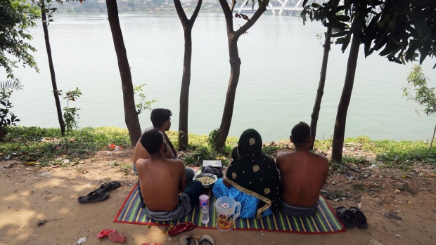 People sit in front of a lake during high temperatures in Dhaka, Bangladesh, on Tuesday, June 6, 2023. Carbon-dioxide emissions from burning fossil fuels are trapping heat in the atmosphere. That's warming the planet and is the primary driver of more extreme weather events, including heat waves.