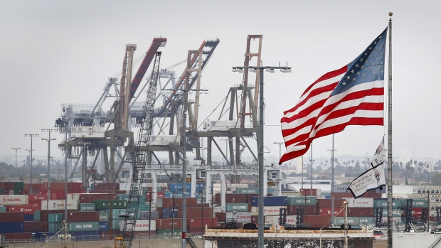 An U.S. flag flies over a baseball field as cranes for unloading shipping containers stand at the Port of Los Angeles in San Pedro, California, U.S., on Monday, June 30, 2014. A six-year labor contract expiring between about 20,000 dockworkers and 29 West Coast ports threatens to disrupt trade as negotiators scramble to forge an agreement on salaries and health-care costs. Photographer: Patrick T. Fallon/Bloomberg via Getty Images