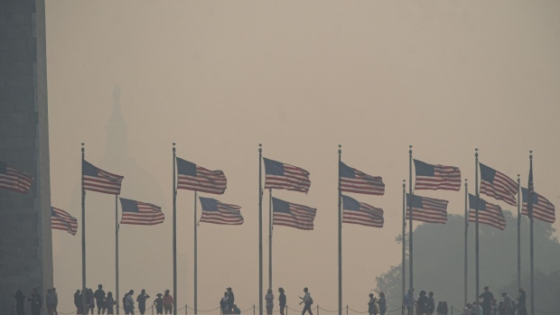 Visitors walk past American flags at the Washington Monument shrouded in smoke from Canada wildfires in Washington on Thursday.
