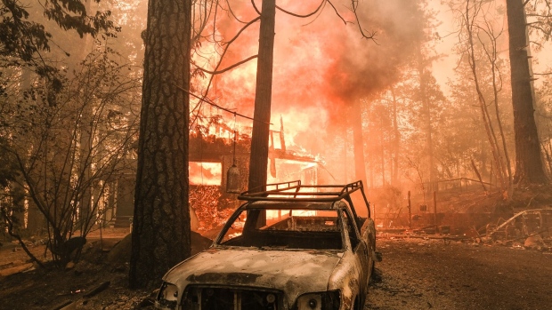 A structure burns behind a charred vehicle on Jerseydale road during the Oak Fire in Mariposa County, California, US, on Saturday, July 23, 2022. A fast-moving wildfire near Yosemite National Park exploded in size Saturday into one of California's largest wildfires of the year, prompting evacuation orders for thousands of people and shutting off power to more than 2,000 homes and businesses.