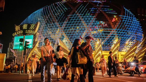 Visitors cross the street in front of the Grand Lisboa casino resort, operated by SJM Holdings Ltd., during Golden Week at night in Macau, China, on Sunday, April 30, 2023. Shares connected to Chinas tourism sector gain as investors position ahead what's expected to be a strong travel season during the five-day Golden Week holiday starting Saturday. Photographer: Eduardo Leal/Bloomberg