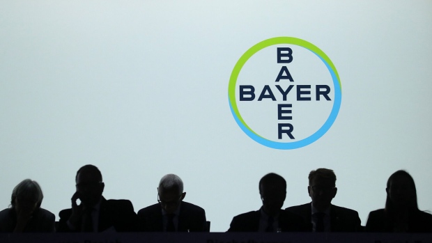 The Bayer AG logo sits on display behind silhouetted members of the management board during the company's annual general meeting in Bonn, Germany, on Friday, May 25, 2018. “We anticipate being able to close the acquisition of Monsanto in the near future,” Bayer Chief Executive Officer Werner Baumann said in statement ahead of the meeting. Photographer: Krisztian Bocsi/Bloomberg