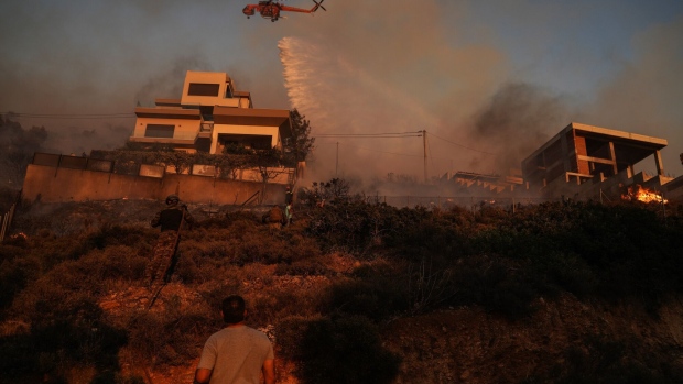 An S-64E Erickson Air-Crane of the Greek fire brigade drops water to extinguish a burning field during a wildfire in Saronida, south of Athens, Greece, on Monday, July 17, 2023. A fire near Athens is threatening homes, as strong winds and high temperatures fuel the blaze.