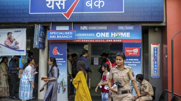 Police officers observe customers standing in line outside a Yes Bank Ltd. branch in Mumbai, India, on Friday, March 6, 2020. India's stock and currency markets tumbled after the central bank seized control of beleaguered Yes Bank, raising concerns about the knock-on effects on the financial system.