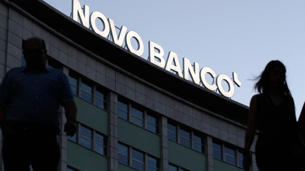 Pedestrians pass an illuminated Novo Banco SA logo above a building in Lisbon, Portugal, on Tuesday, Aug. 11, 2015. The Bank of Portugal's Resolution Fund owns Novo Banco after the 4.9 billion-euro ($5.4 billion) bailout, and the rescue will be repaid by proceeds from the sale. Photographer: Thomas Meyer/Bloomberg