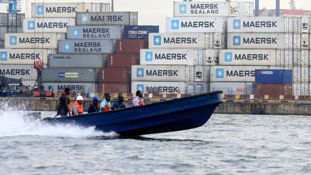 People ride on a boat past A.P. Moeller-Maersk A/S branded shipping containers stacked at the Ladol free trade zone port in Lagos, Nigeria, on Tuesday, May 22, 2018. Ladol, a logistics hub for the offshore oil industry in Lagos, Nigeria, is mulling a stock-market listing and corporate bonds to expand its facilities and get more business from major production companies.