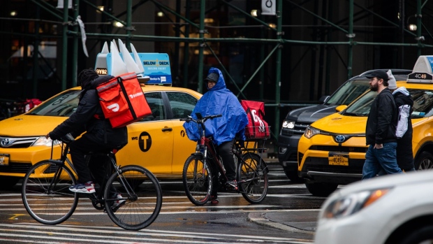 Food delivery workers on bicycles travel along a street in New York, U.S., on Tuesday, March 17, 2020. In New York City, the virtual shutdown from the coronavirus pandemic is threatening to create massive holes in the budget as billions of dollars in tax revenue disappears.