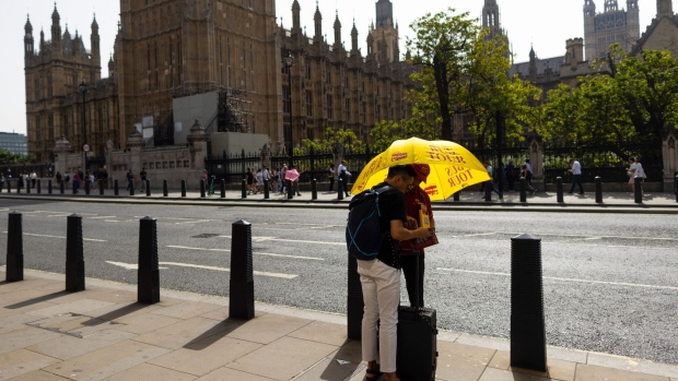 A tourist speaks with a tour guide under the shade of an umbrella, near the Houses of Parliament, during hot weather, in London, UK, on Wednesday, Sept. 6, 2023. London will exceed 30C (86F) on Wednesday, with an autumnal heat wave searing northwest Europe while storms and floods batter the Mediterranean.