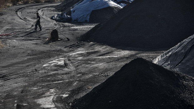 A man walks past piles of coal at the Qinhuangdao Port in Qinhuangdao, China, on Friday, Oct. 28, 2016. China's efforts to quell surging coal prices showed signs they’re working, with benchmark prices dropping for the first time in a year as the country's production rose to the highest in seven months. Photographer: Qilai Shen/Bloomberg