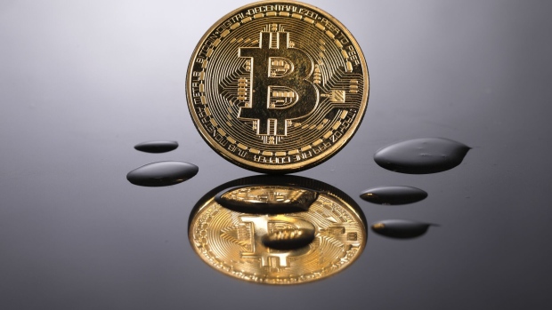 A coin representing Bitcoin cryptocurrency is reflected on a polished surface as it sits in a pool of translucent liquid in the U.K. Photographer: Bloomberg Creative Photos/Bloomberg