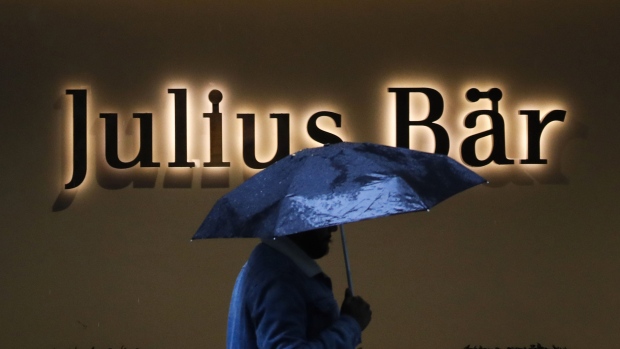 A pedestrian beneath an umbrella passes a Julius Baer Group Ltd. branch in Zurich, Switzerland, on Tuesday, July 13, 2021. UBS Group AG and Julius Baer report earnings this week.