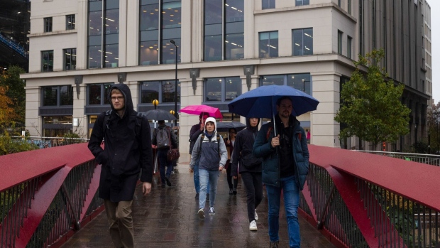 Commuters shelter from the rain under umbrellas as they walk over the Esperance Bridge crossing a canal near the King's Cross development in London, UK, on Tuesday, Nov. 15, 2022. Britain's job shortages showed no signs of easing in the third quarter as more people dropped out of work and wages grew at the fastest pace in over a year, adding to inflationary concerns for the Bank of England. Photographer: Carlos Jasso/Bloomberg
