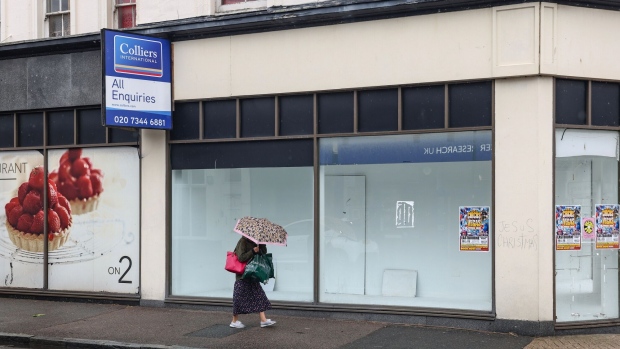 A woman passes a vacant retail unit on the high street in Eastbourne, UK. hotographer: Hollie Adams/Bloomberg