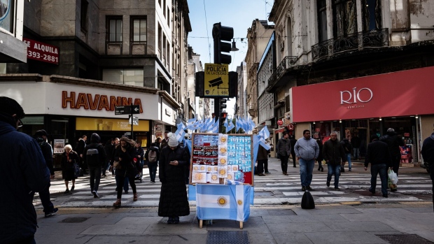 Pedestrians walk past a vendor selling Argentine flag souvenirs on the street in Buenos Aires, Argentina, on Tuesday, Aug. 13, 2019. In the wake of President Mauricio Macri's stunning rout in primary elections over the weekend, investors dumped its stocks, bonds and currency en masse, leaving much of Wall Street wondering whether the country was headed for yet another default. Photographer: Erica Canepa/Bloomberg