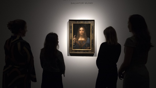 Staff members pose next to the 'Salvator Mundi' by Leonardo di Vinci in London. Photographer: Carl Court/Getty Images