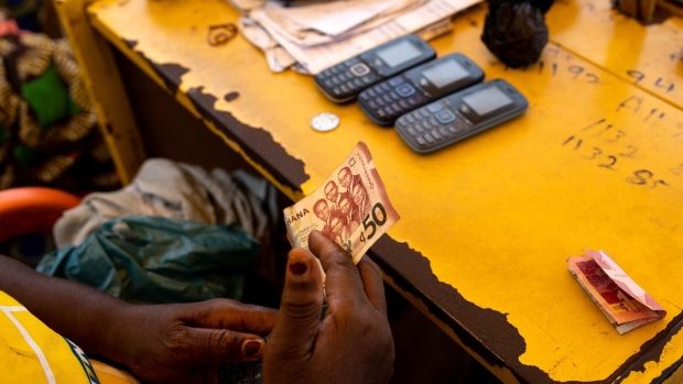 A mobile money kiosk worker hands a Ghana fifty cedi banknote to a customer in Accra, Ghana, on Tuesday, Feb. 28, 2023. Ghana’s cedi, the world’s second-worst performing currency this year, is heading for more pain after the West African nation missed a self-imposed deadline to restructure its bilateral debt and move closer to tapping foreign aid. Photographer: Ernest Ankomah/Bloomberg