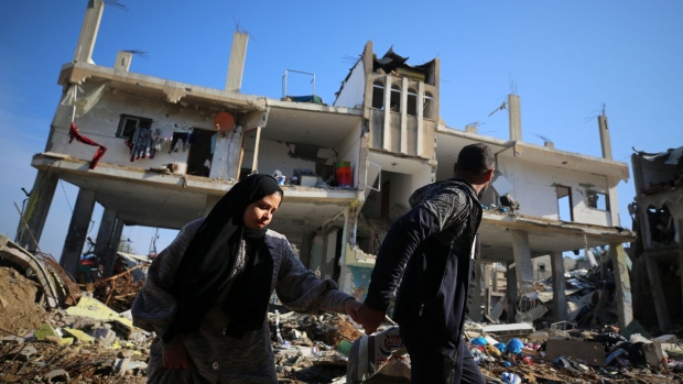 Palestinian people walk past a destroyed building in the Al-Maghazi refugee camp in Gaza, on Jan. 16. Photographer: -/AFP/Getty Images