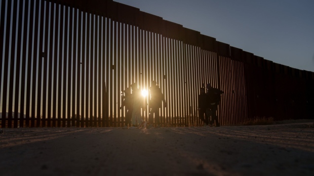 Migrants walk along the US-Mexico border fence in Lukeville, Arizona, US, on Tuesday, Dec. 12, 2023. An influx of migrants crossing the border unlawfully around remote Lukeville, Arizona, has overwhelmed US border officials causing them to close the official port of entry in order to direct resources to processing the unlawful arrivals. Photographer: Eric Thayer/Bloomberg
