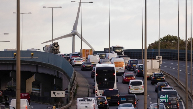 Vehicles travel along the A13 arterial road against the backdrop of a wind turbine in London, UK, on Monday, Nov. 13, 2023. A levy on drivers of older cars with dirtier engines has pushed many of them off London’s roads, reducing pollution that’s been blamed for thousands of deaths in the capital each year. Photographer: Chris Ratcliffe/Bloomberg