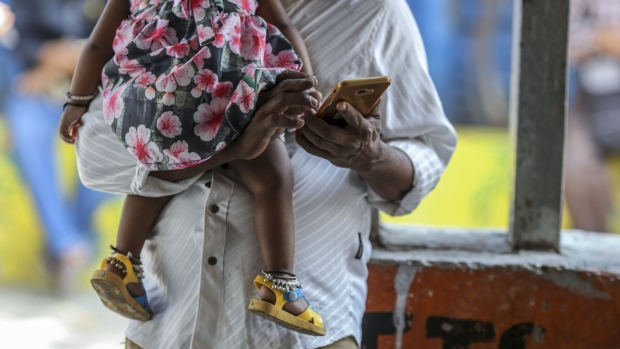 A man uses a smartphone while carrying a child in Mumbai, India, on Saturday, Feb. 15, 2020. Facebook, YouTube, Twitter and TikTok will have to reveal users' identities if Indian government agencies ask them to, according to the country’s controversial new rules for social media companies and messaging apps expected to be published later this month.