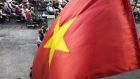 A Vietnamese national flag flies as motorcyclists wait at a traffic signal in Ho Chi Minh City, Vietnam, on Friday, Jan. 12, 2018. A global trade recovery and Vietnam’s young and low-cost workforce have been magnets for international investors like Nestle SA, which have opened factories in the country this year. That’s helping underpin its economy, which expanded 6.8 percent in 2017, among the fastest in the world. Photographer: Ore Huiying/Bloomberg