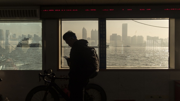 A passenger is silhouetted as he looks at a mobile phone on a ferry crossing the Yangtze River in Wuhan, Hubei, China, on Wednesday, Dec. 11, 2019. China's economic growth will come in at 5.9% in 2020 as easing trade tensions and the prospect of lower bank borrowing costs boost confidence, according to analysts and traders. Photographer: Qilai Shen/Bloomberg