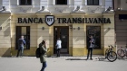 <p>Pedestrians pass a Banca Transilvania SA bank branch in Timisoara, Romania.</p>