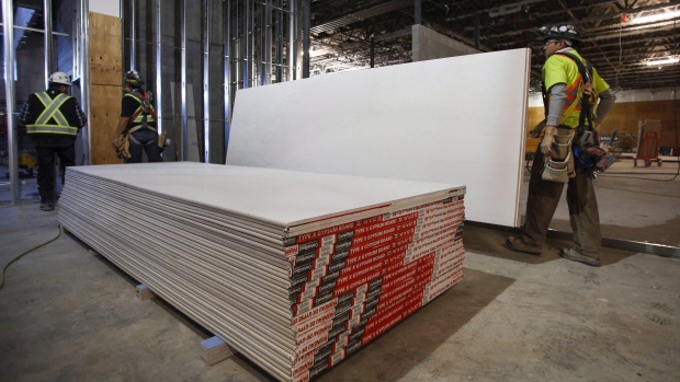 Construction workers move sheets of drywall at a building project in Calgary.