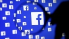 A man poses with a magnifier in front of a Facebook logo on display