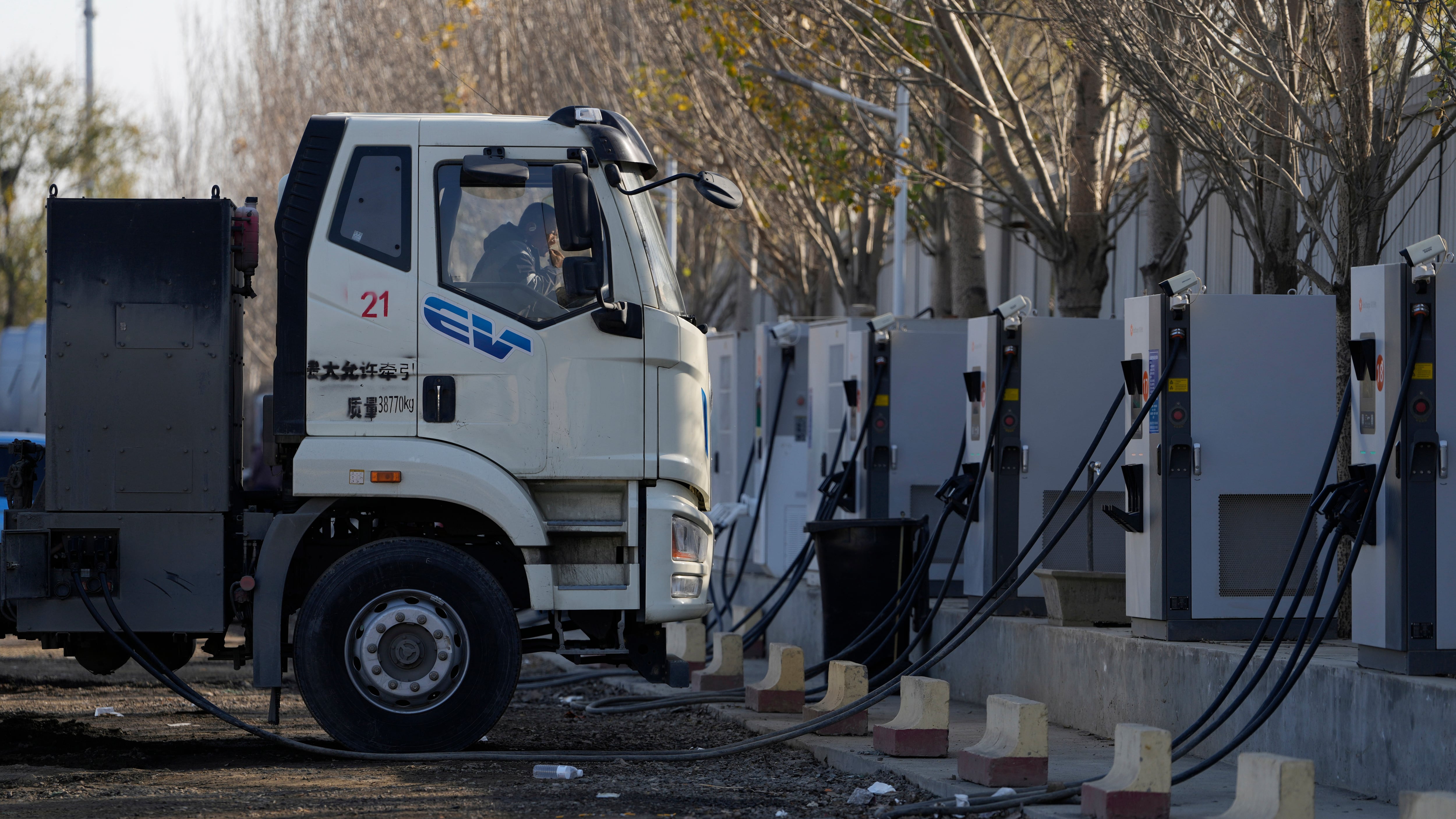 A driver rests in the cabin as his electric truck is plugged into a charging station on the outskirts of Beijing on Nov. 14, 2025. (Ng Han Guan / AP Photo)