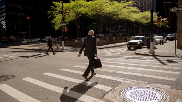 A pedestrian carrying a briefcase crosses a street in the Financial District of New York, U.S., on Wednesday, May 12, 2021. With 37% of Manhattan fully vaccinated, the city's finance industry, slowly, is getting back into the office. Photographer: Amir Hamja/Bloomberg